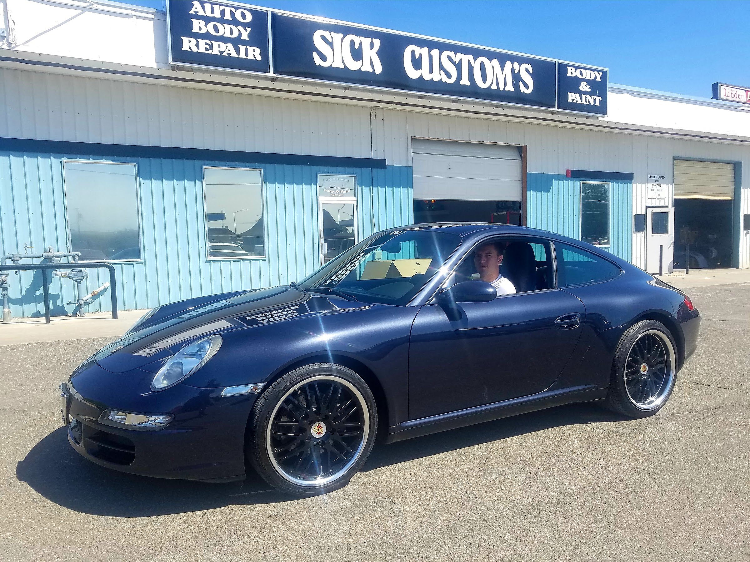 A dark blue Porsche 911 outside the Sick Custom Collision shop