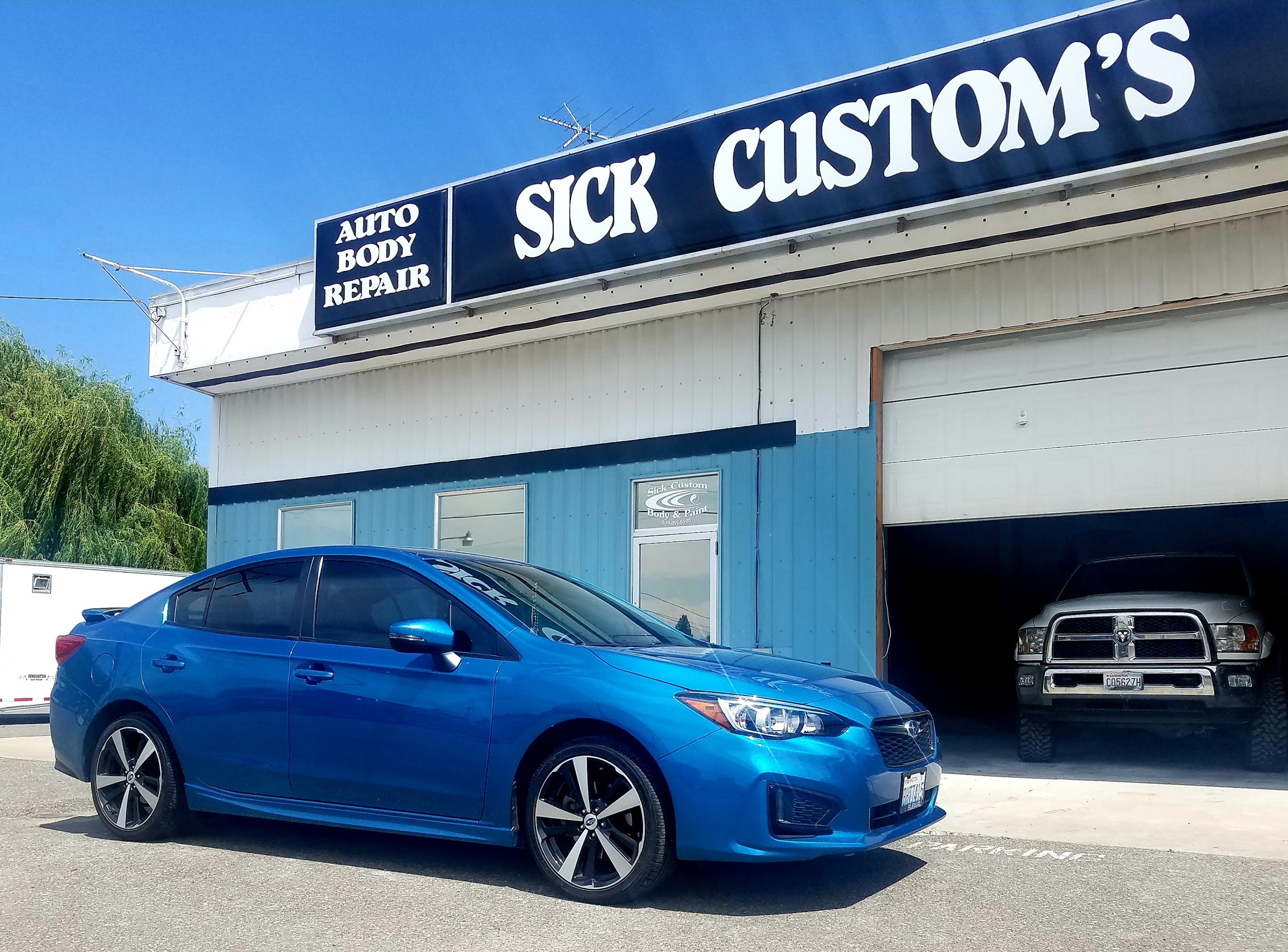 A bright blue Subaru Impreza in front of the Sick Custom Collision storefront