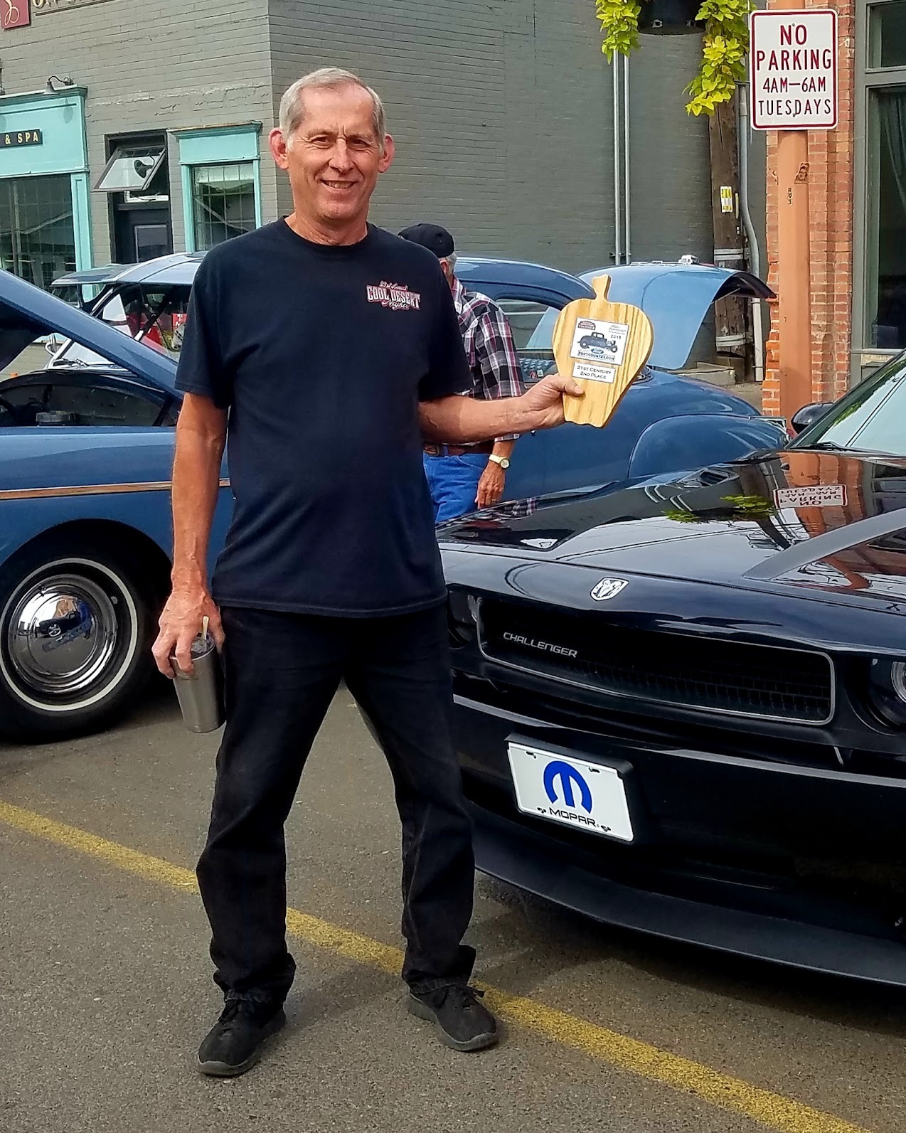 Wayne, owner of Sick Custom Collision Repair, holding a car show award beside a custom Dodge Challenger